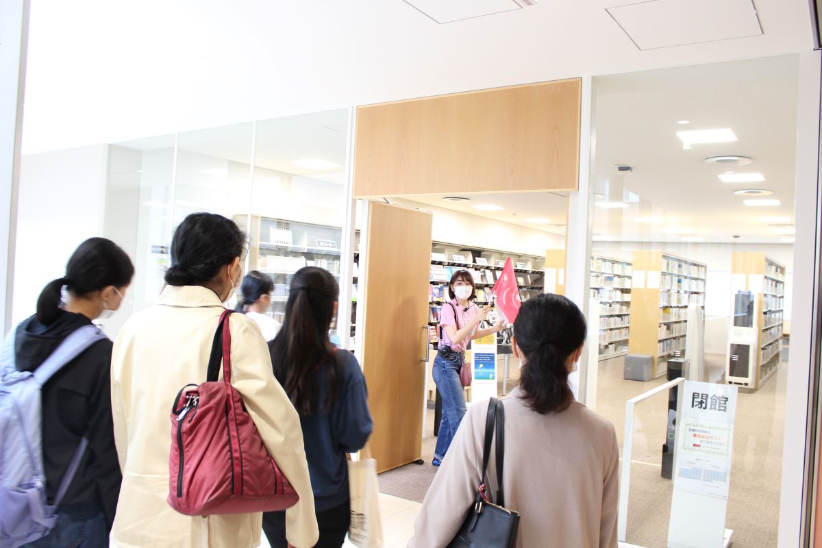 写真：キャンパスツアーの様子。千駄ヶ谷の図書館入口で学生スタッフが説明をしている。