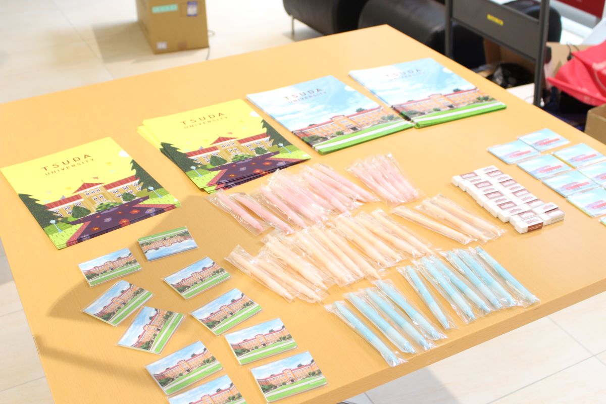 写真：津田塾のノベルティグッズが机上に置かれている。奥にクリアファイル2種類。手前は左から、ポケットティッシュ、シャープペンシル、消しゴム等。