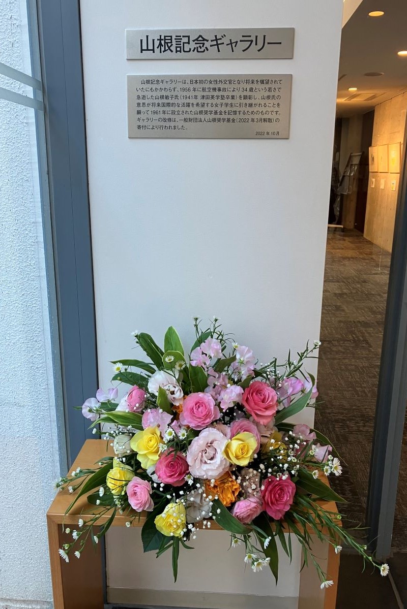 写真：山根記念ギャラリー入口。画面上に、山根記念ギャラリーのプレート。画面下に、お祝いの花束。