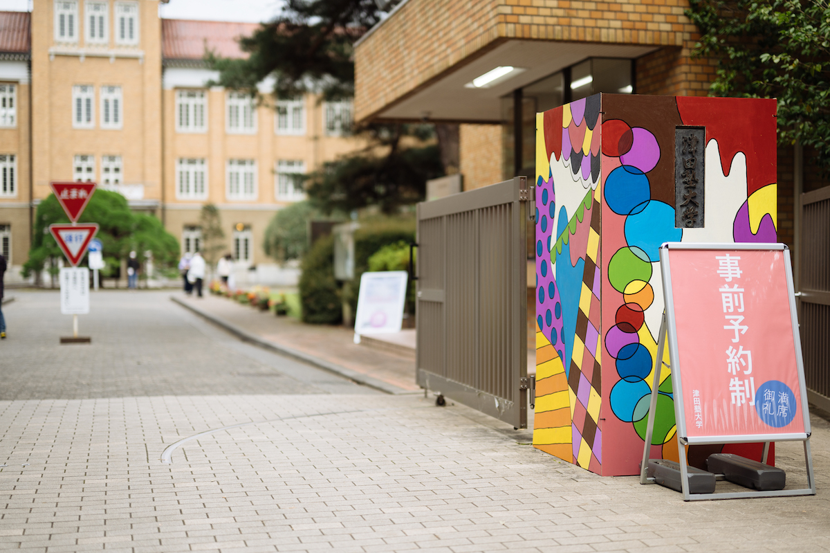 写真：塾祭当日の正門。メインテーマらしいビビットカラーの模様のイラストで門が飾られている。