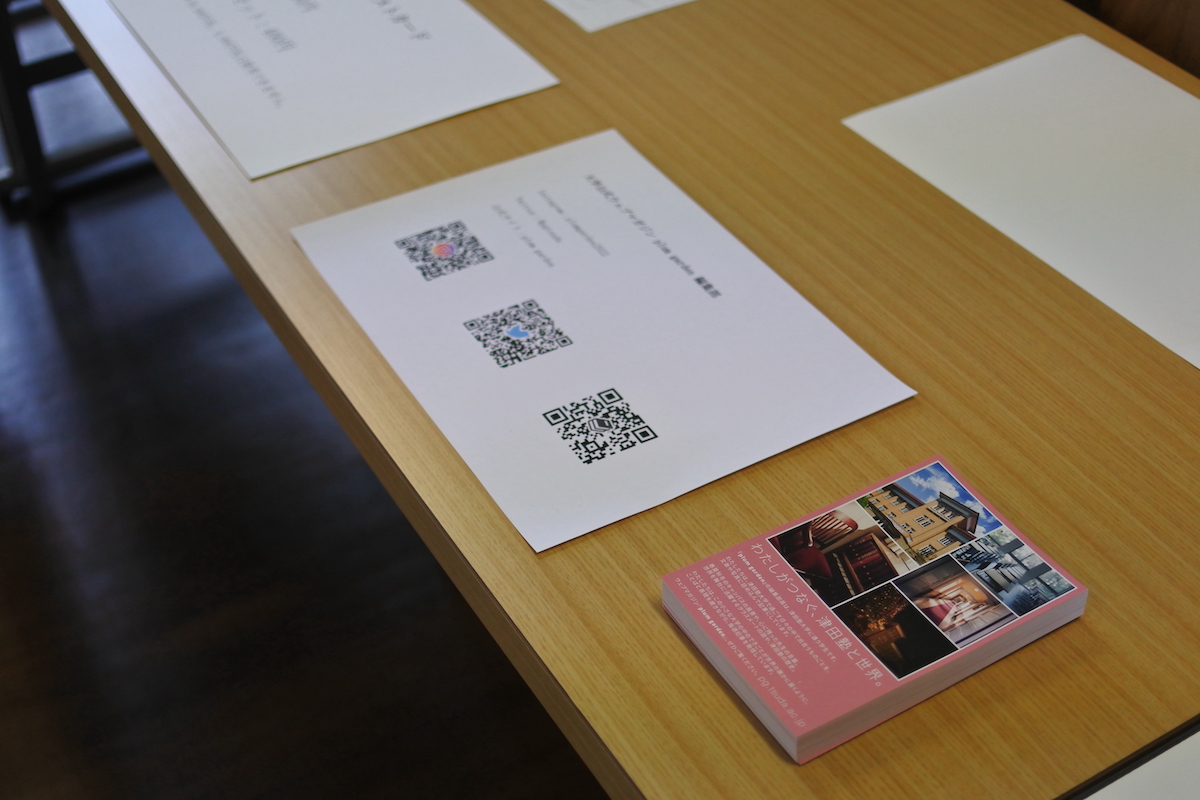 写真：plum garden 編集部 の受付机に、左にSNSのQRコード、右にポストカードが置かれている。
